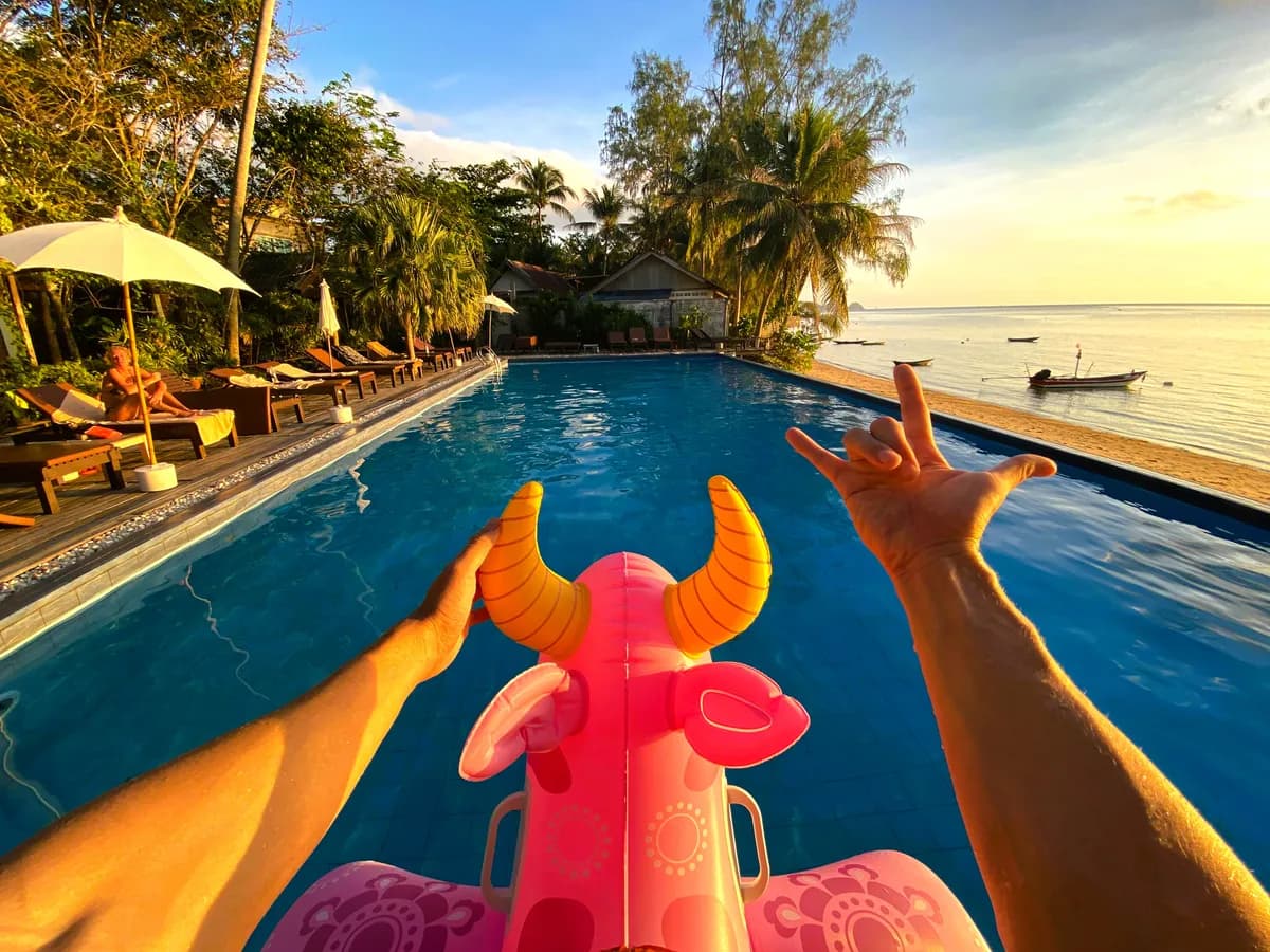 Traveler floating on a pink inflatable in a beachfront pool at sunset